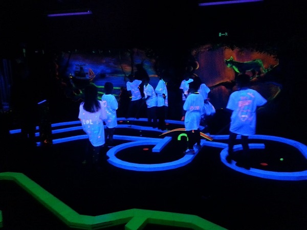 tieners spelen minigolf in Blacklight met witte t-shirts aan